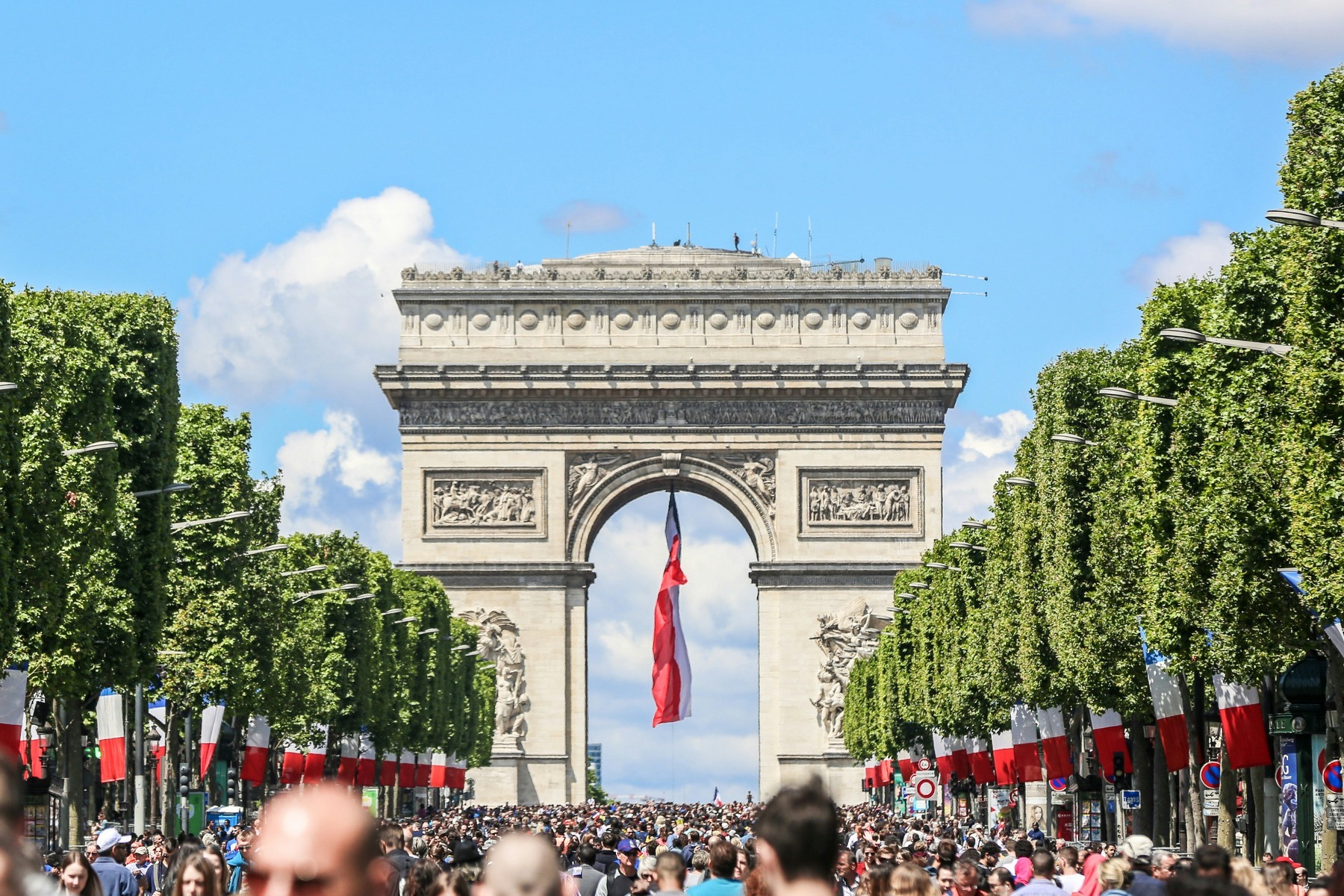 Crowds on the Champs-Élysées beneath the Arc de Triomphe, draped with a giant French tricolour flag, on Bastille Day in Paris