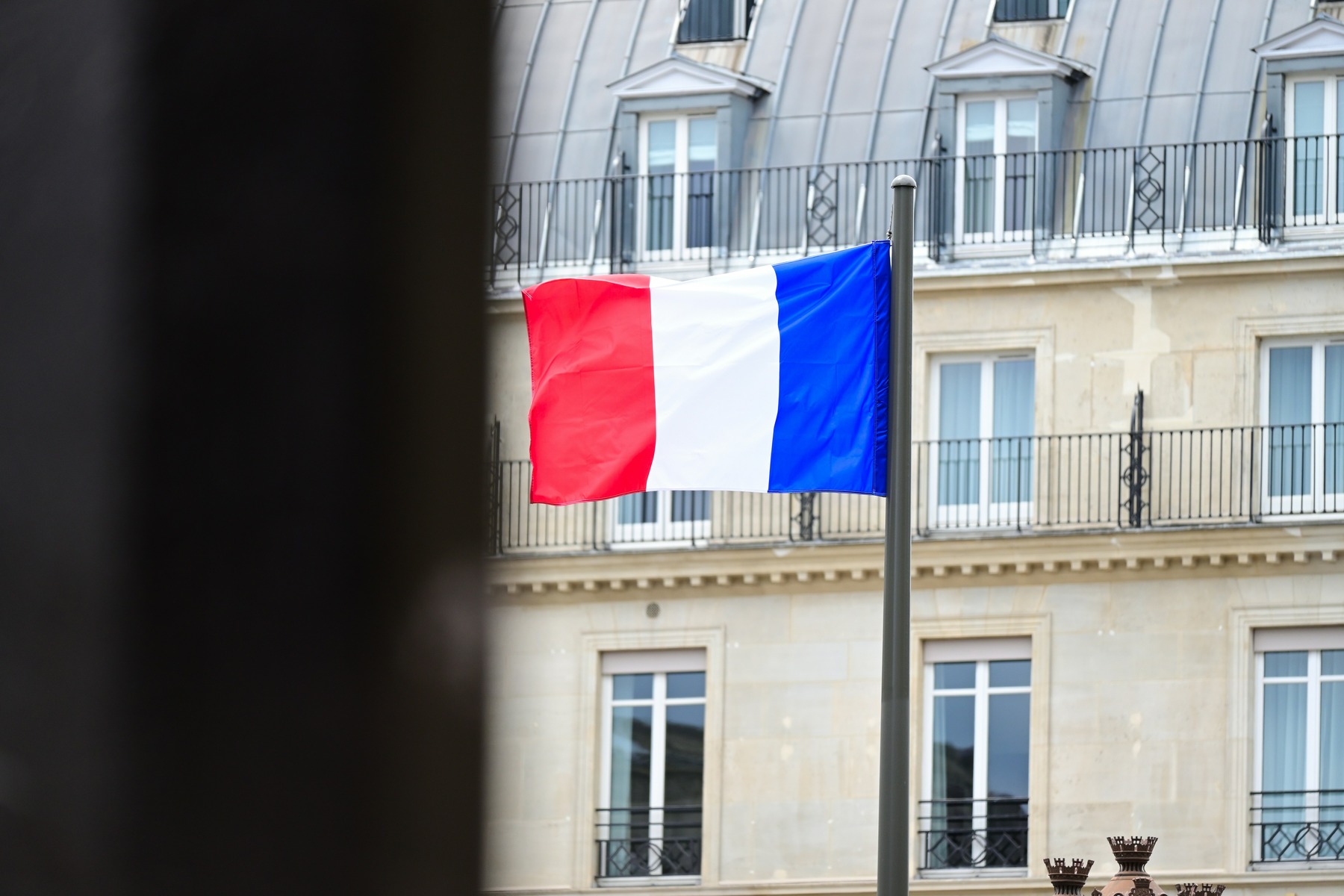A French tricolour flag flying from a Haussmann building in Paris during the Bastille Day national holiday