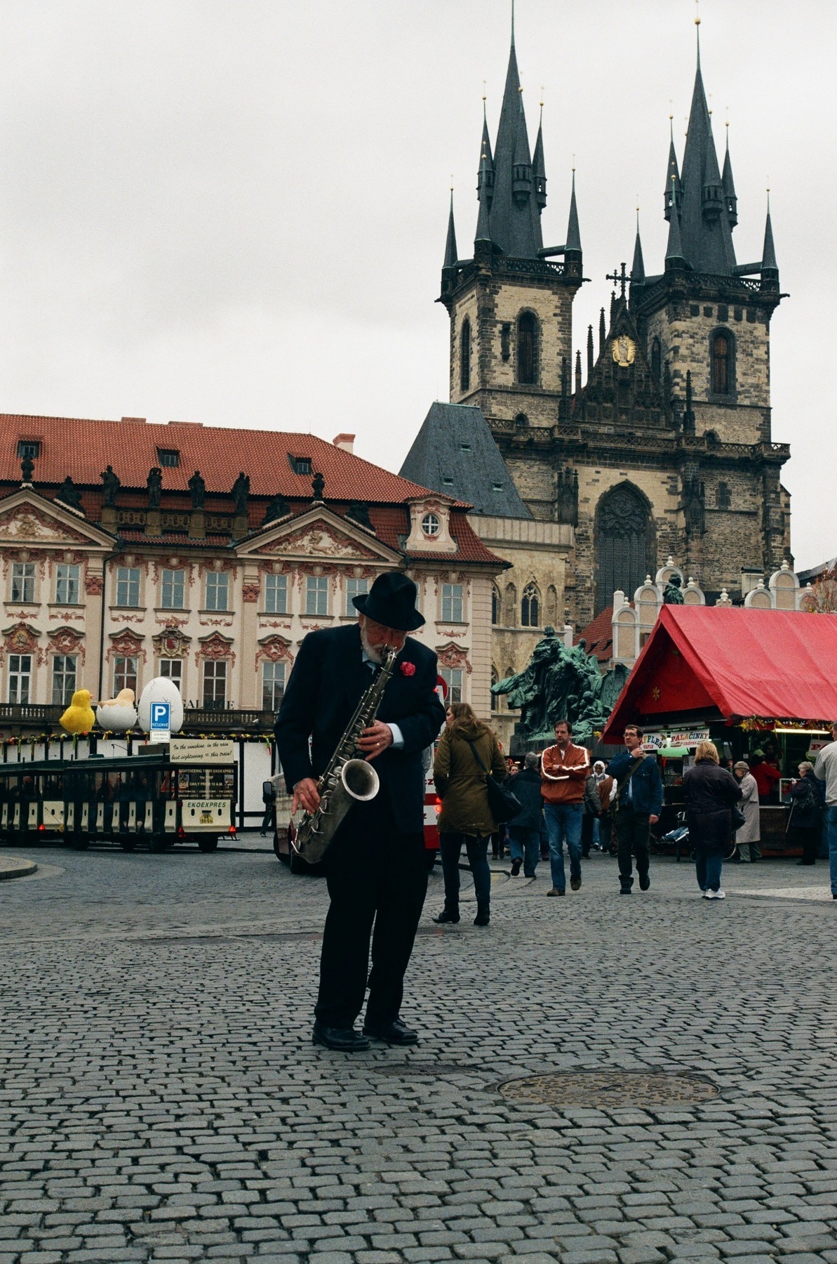 A saxophonist playing in Prague's Old Town Square with the towers of the Týn Church behind