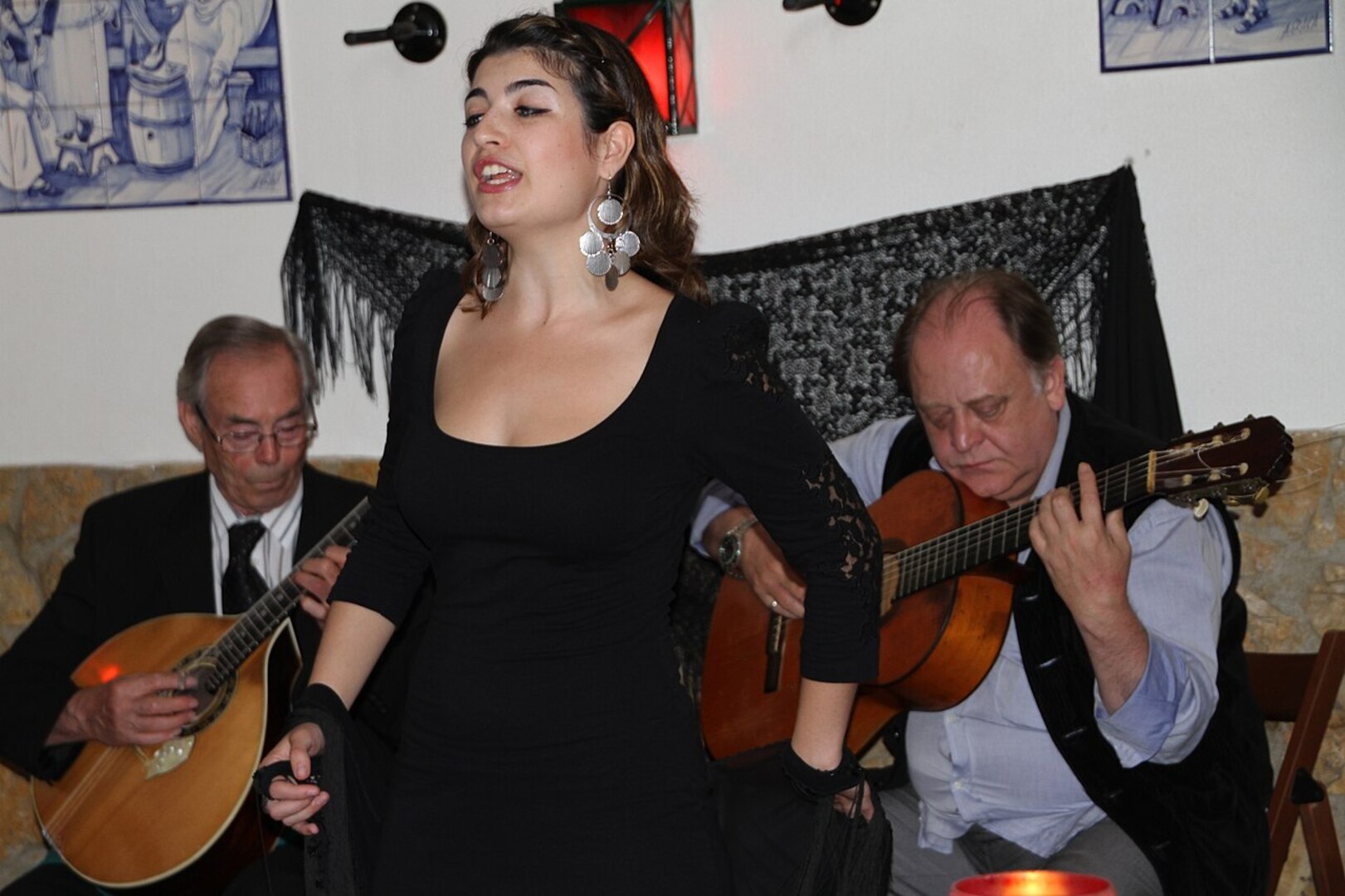 A fado singer in black performing in a candlelit tavern in Alfama, Lisbon, accompanied by Portuguese guitar