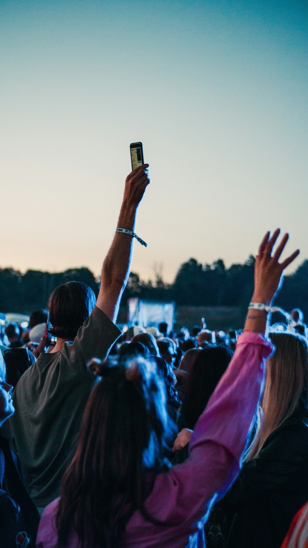 Festival-goers with raised hands and phones in the crowd at dusk during Lollapalooza Paris