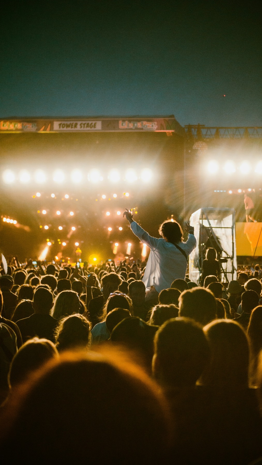 A vast festival crowd facing a brightly lit main stage at night during Lollapalooza Paris