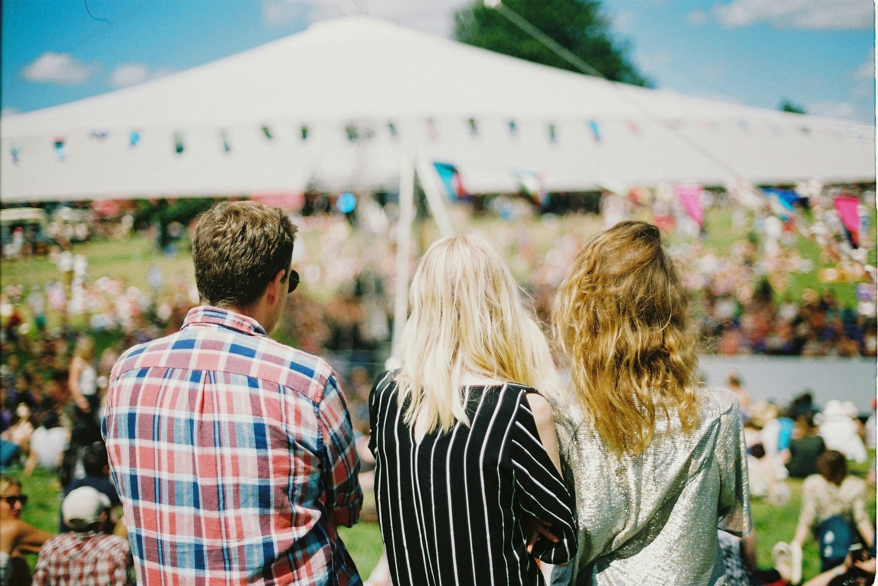 Festival-goers watching the main stage from a grassy field on a sunny festival day