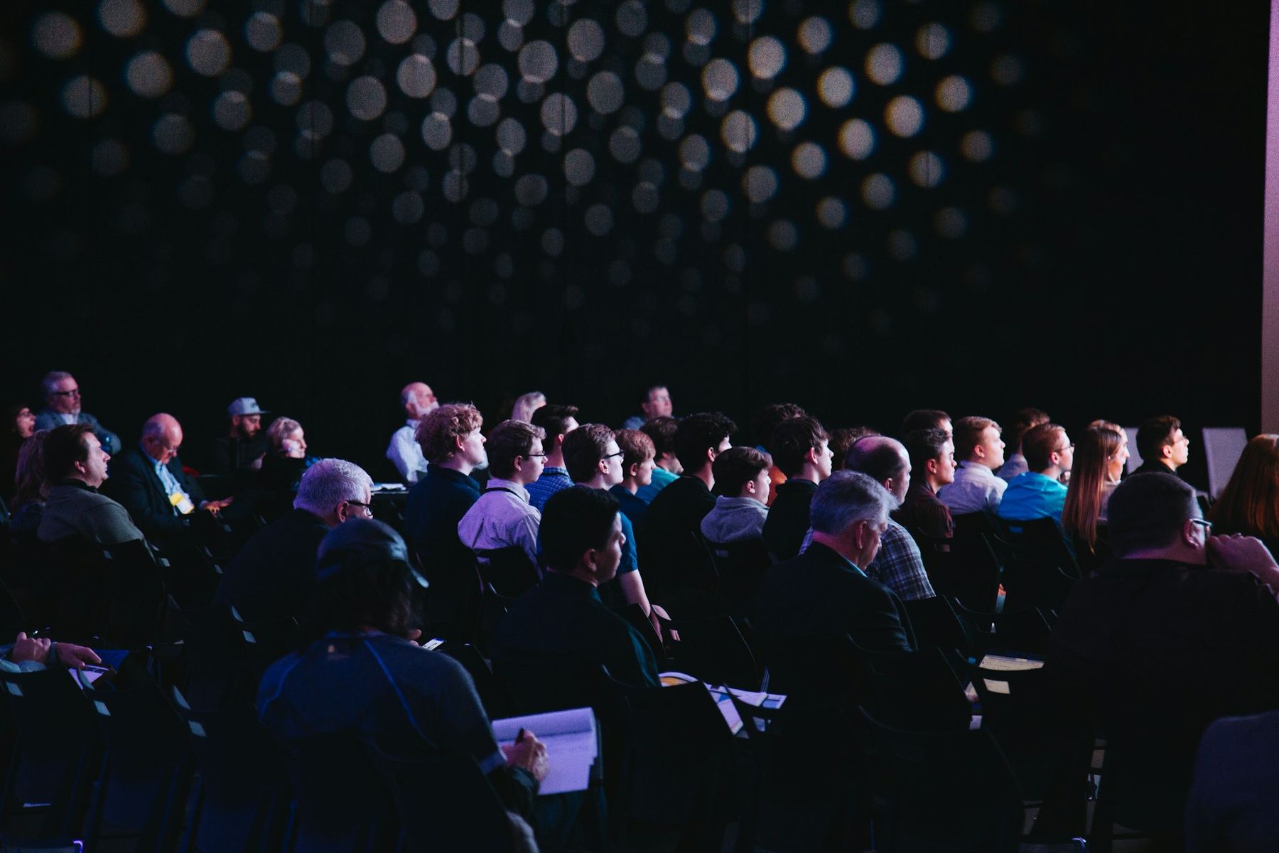 Rows of attendees listening to a session in a darkened conference auditorium