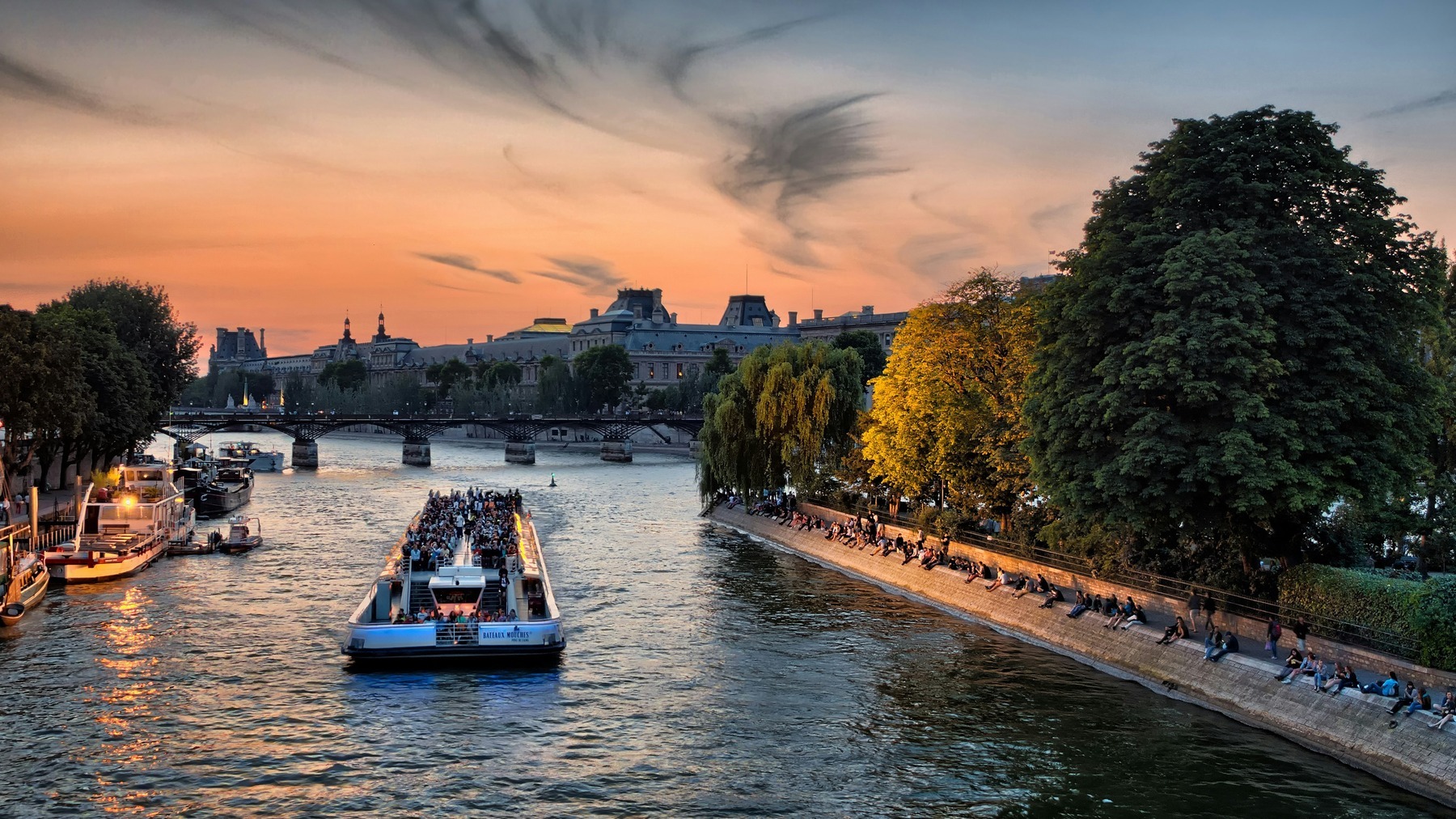 The Seine at sunset with a sightseeing boat and people relaxing along the riverbank during Paris Plages