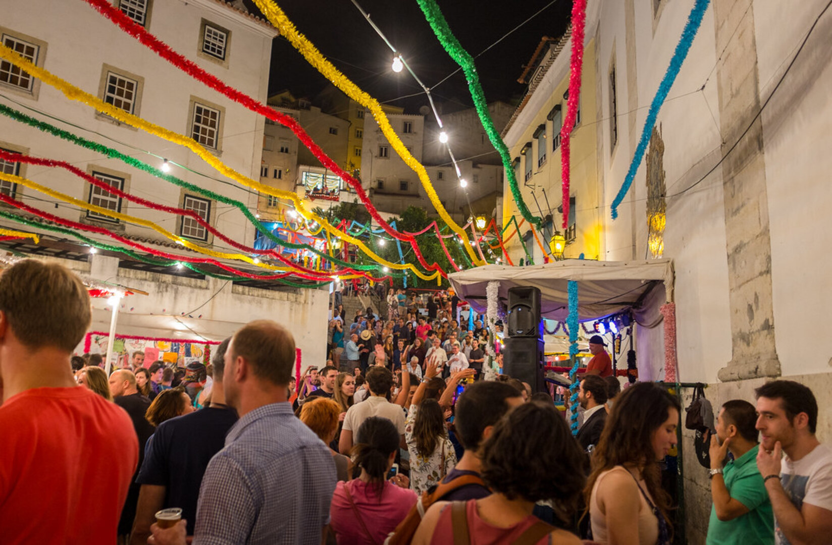 A neighborhood arraial in Lisbon during Santos Populares, with outdoor tables, colored lights, and music