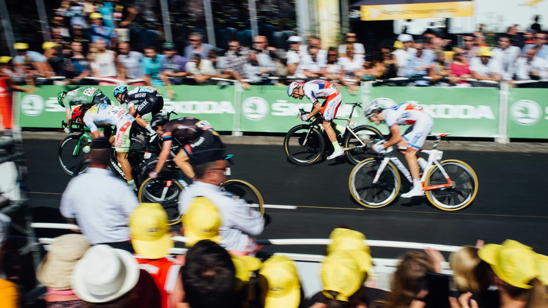 Tour de France riders sprinting toward the finish line as spectators watch from behind the barriers