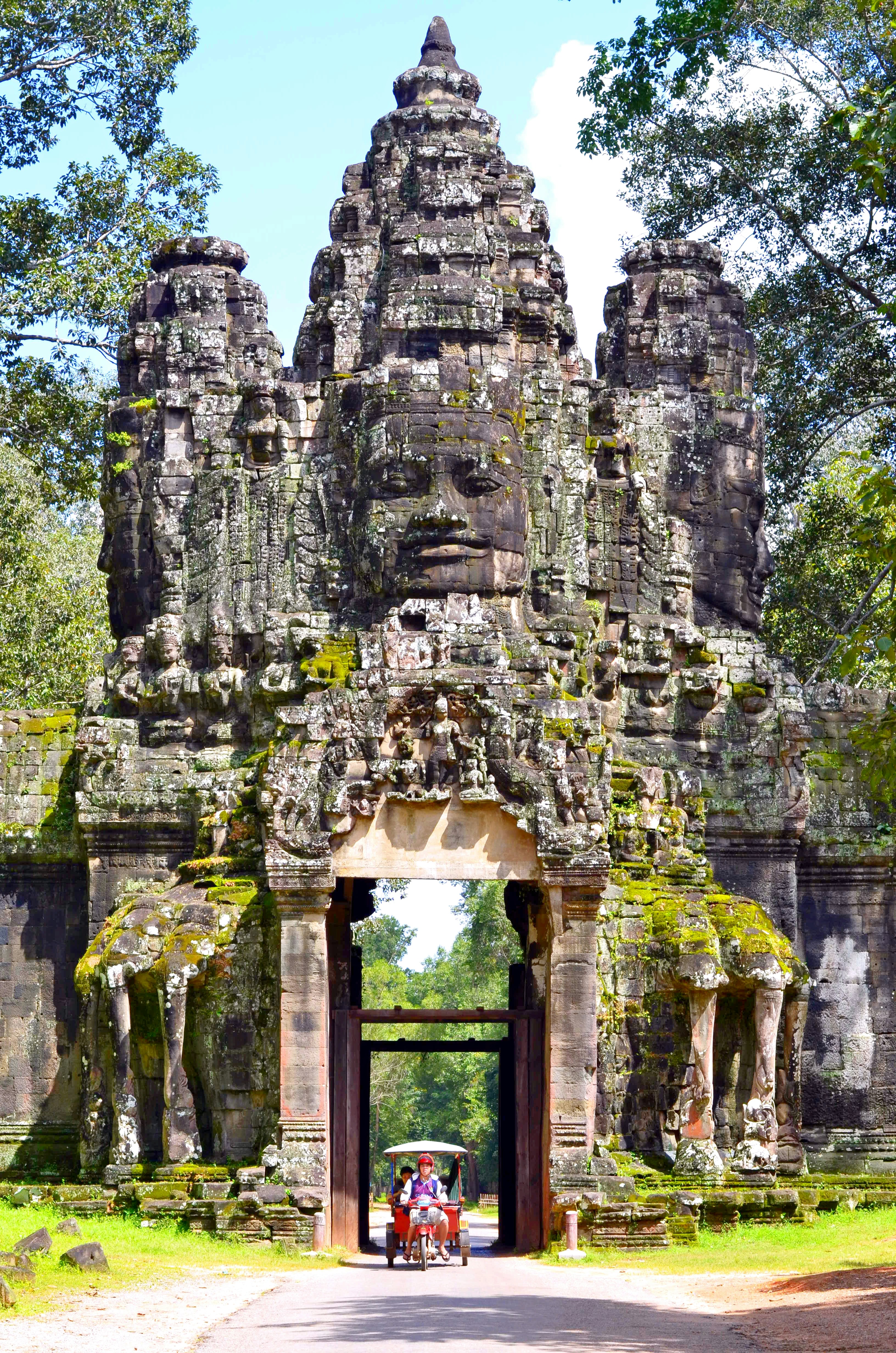 A tuk-tuk passing beneath the face tower of an Angkor Thom gate