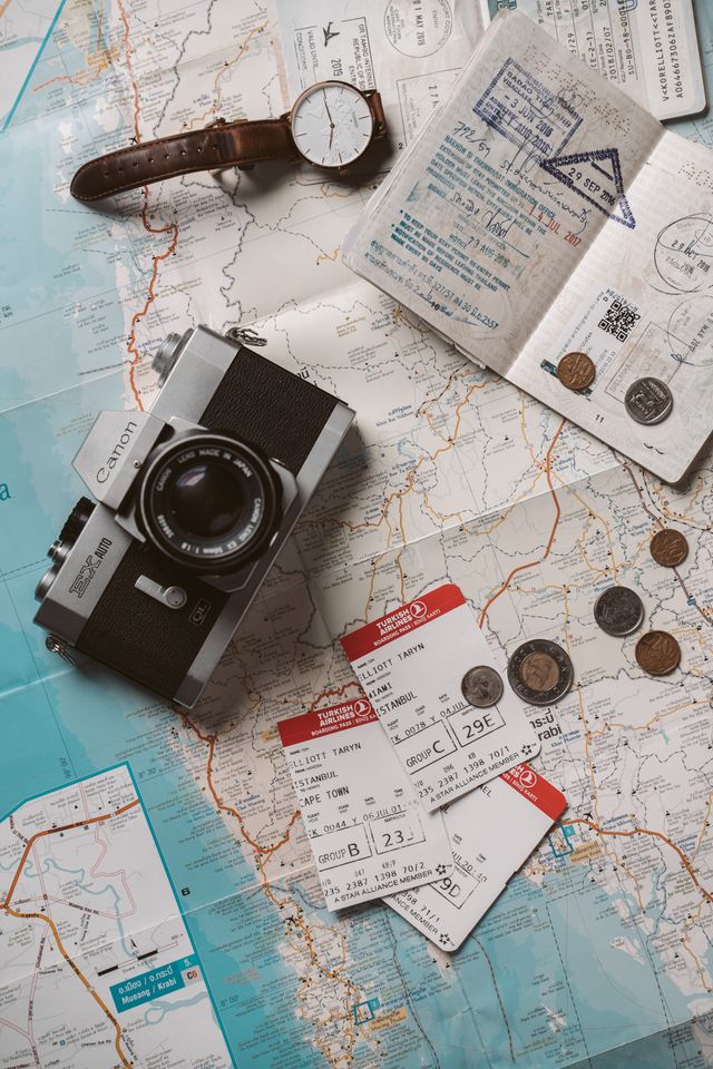 Travel essentials laid out on a map: passport, boarding passes, camera, and coins